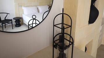 Une salle de bain avec un miroir rond, un lit, une petite table ronde et un panier en osier.