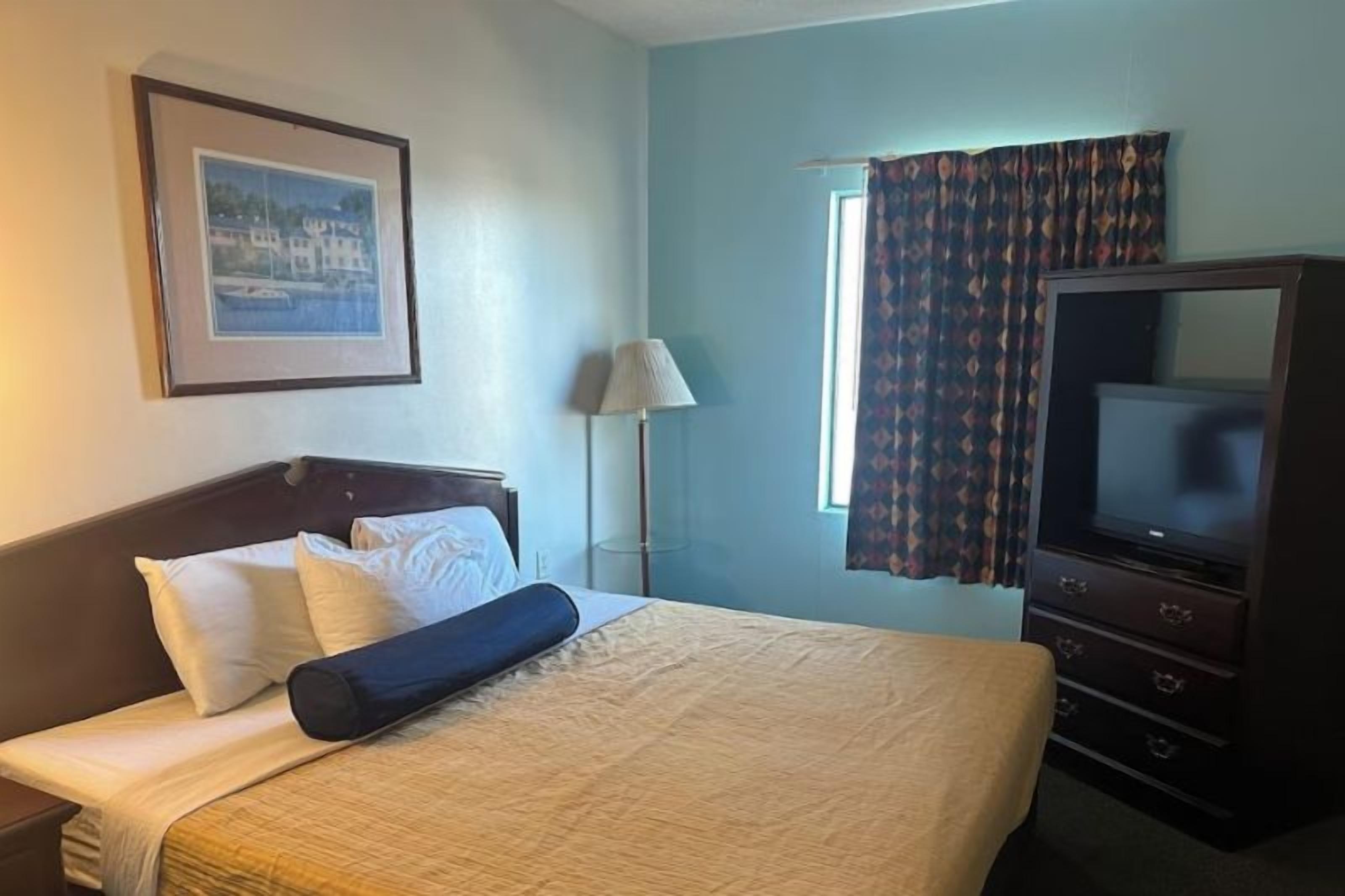 A hotel room with a bed, a television, a lamp, and a window with curtains.