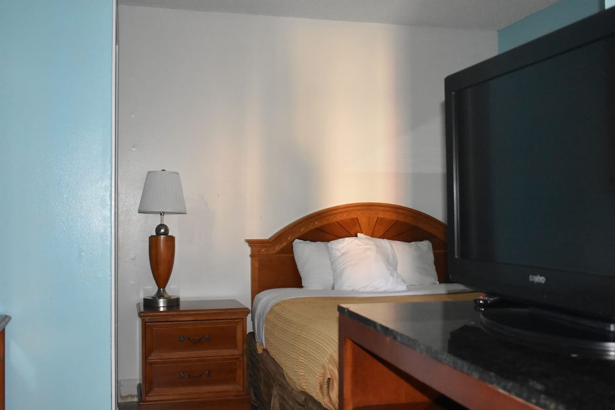 Une chambre d’hôtel comprenant un lit, une télévision, une table de chevet avec une lampe et une commode.