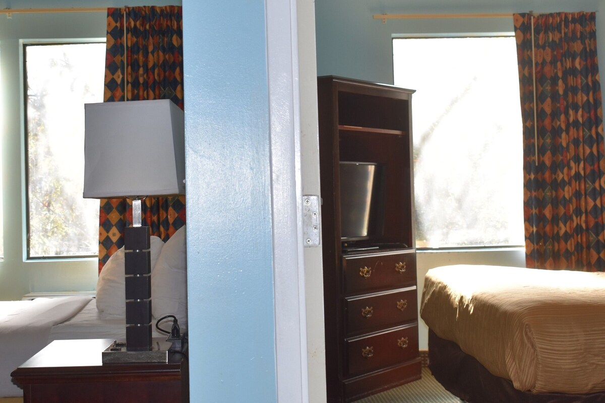 A hotel room with a bed, a desk with a lamp, a wardrobe, and curtains.