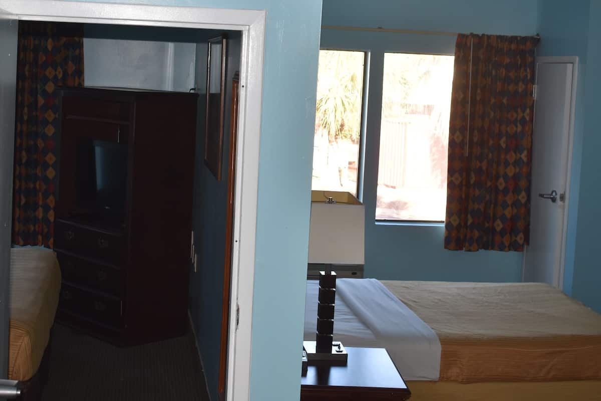 Une chambre avec un lit, une petite table, une télévision et une fenêtre avec des rideaux.