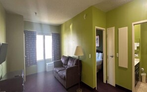 A room with a sofa, a lamp, a television, and a door leading to a bathroom. - GUEST COTTAGES & SUITES (Brunswick)