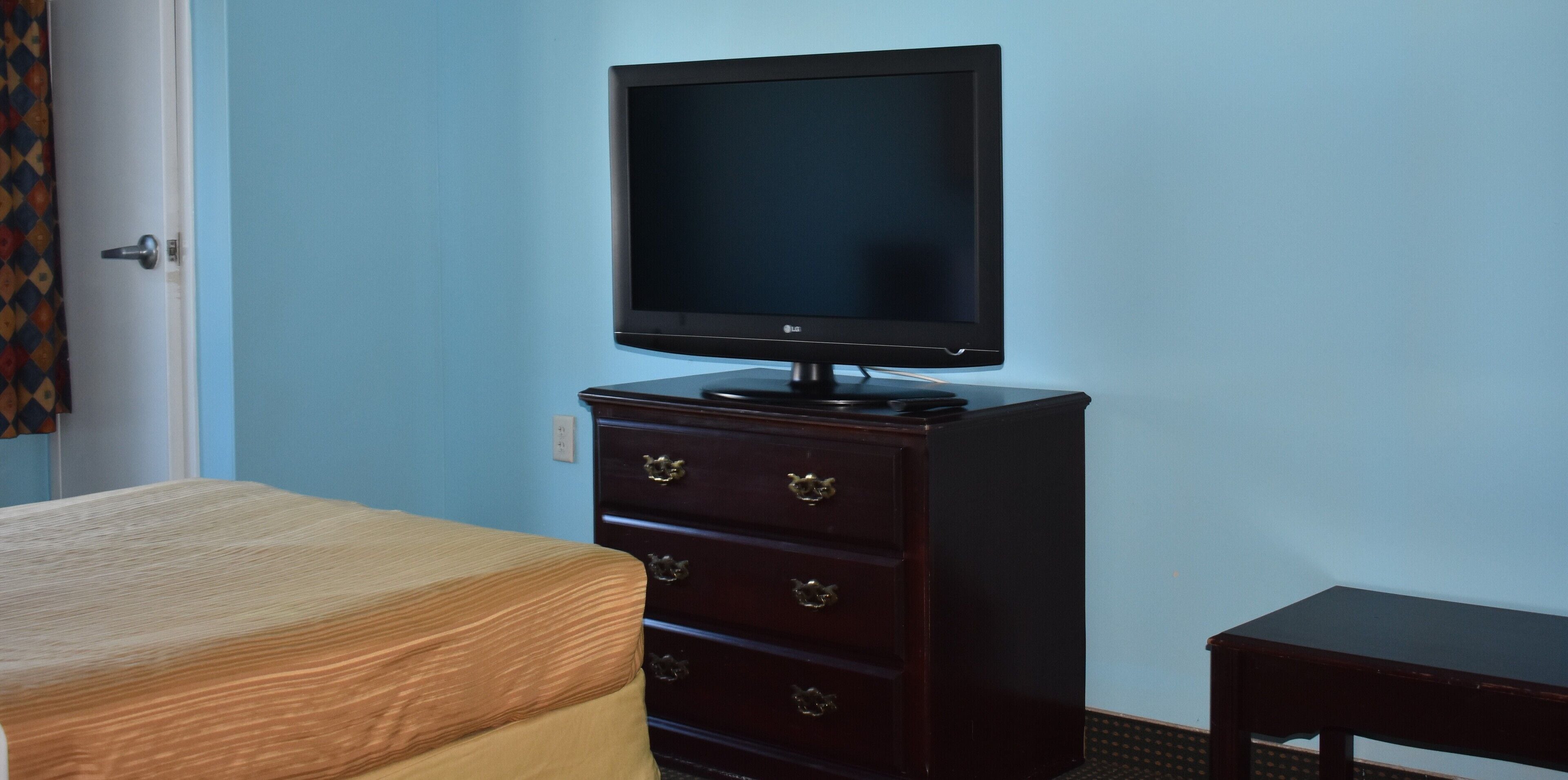 A room with a bed, a dresser with drawers, a television on top, and a small table.