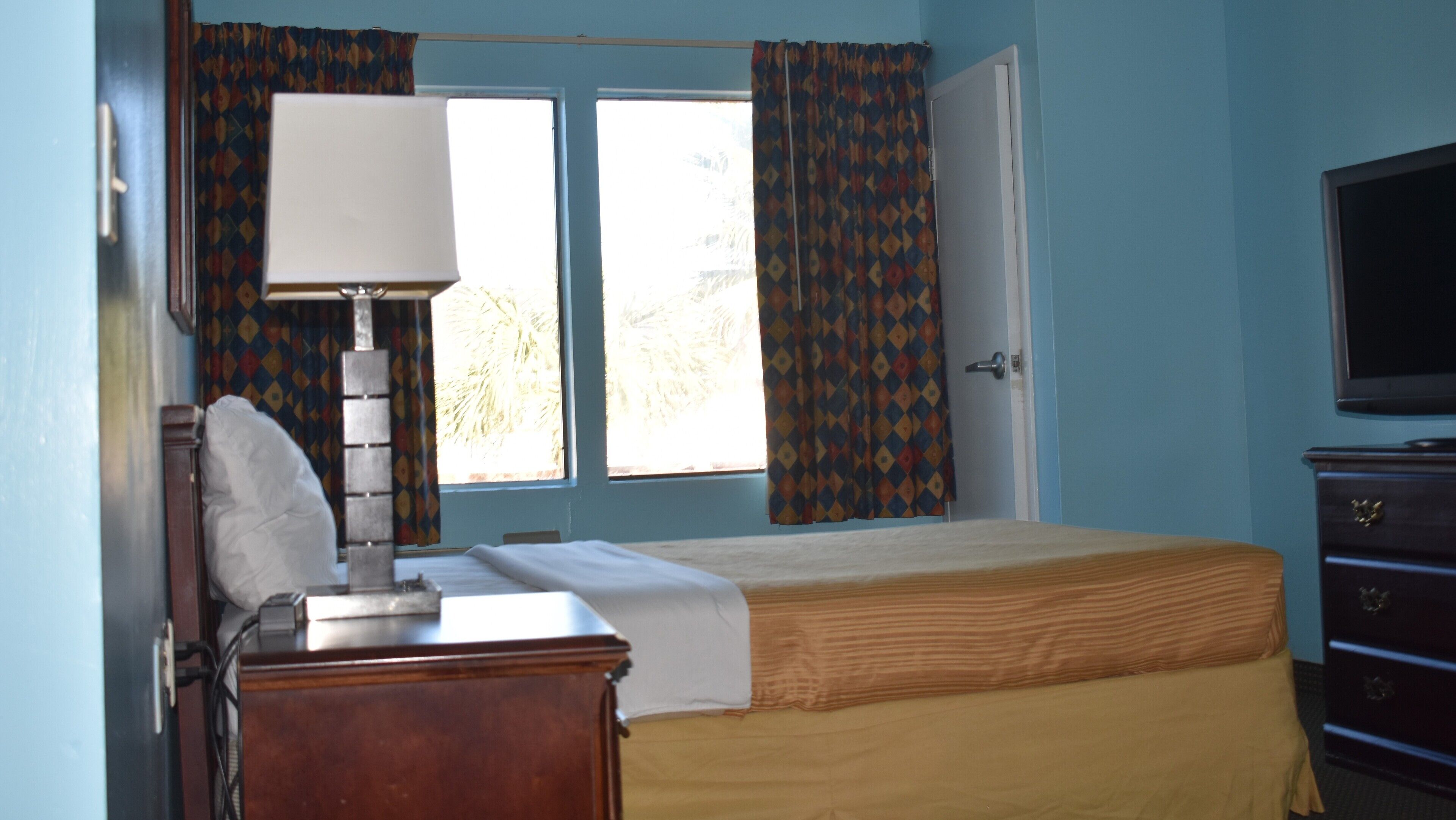 A bedroom with a bed, a desk, a chair, a television, and curtains.