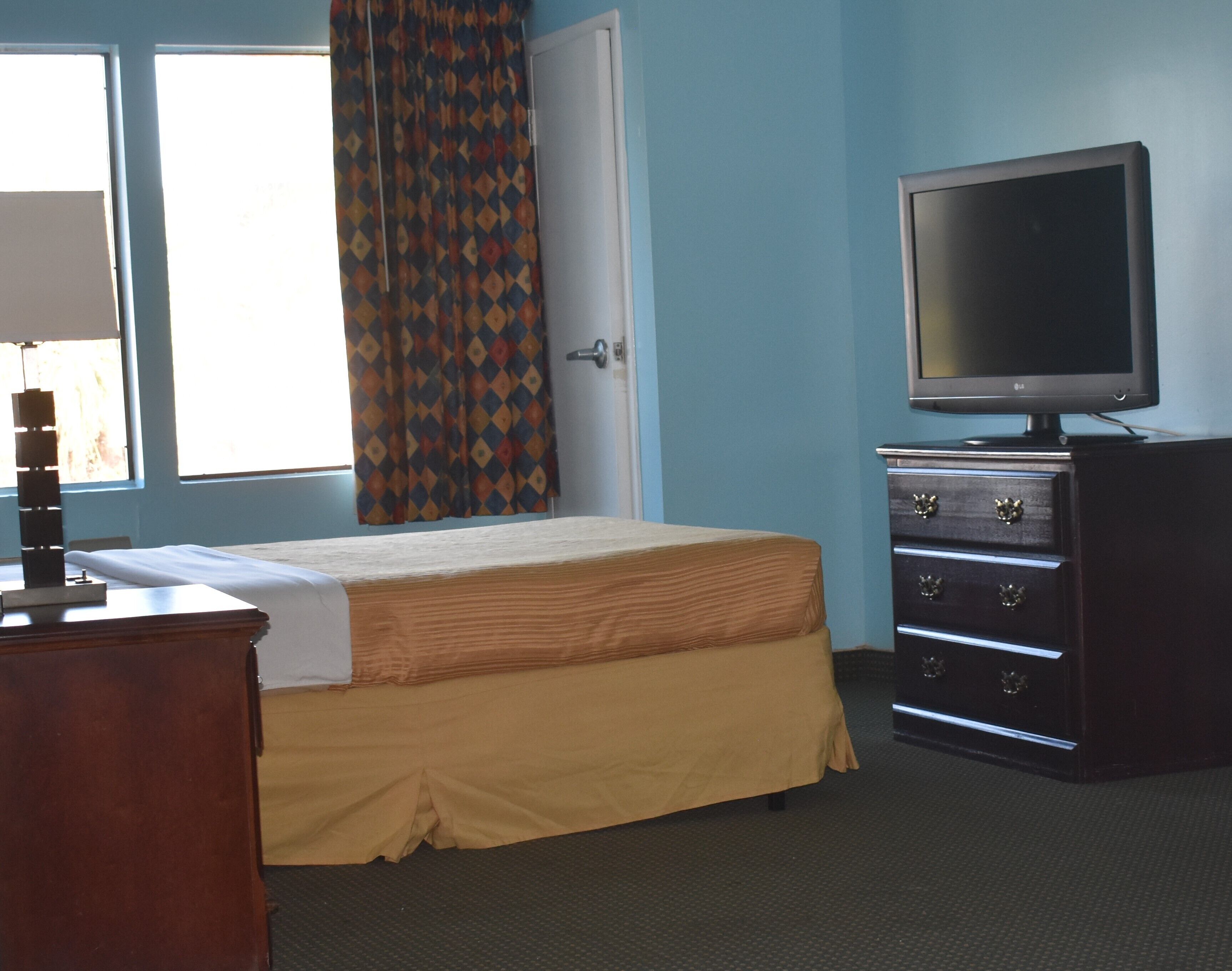 A bedroom with a bed, a dresser, a television, and a window with curtains.