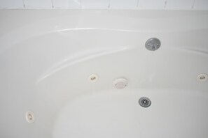 A white bathtub with a drain, a plug, and a control knob. - GUEST COTTAGES & SUITES (Brunswick)