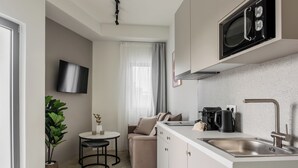 A modern kitchen with a built-in microwave, a sink, and a coffee maker. There is a small dining area with a table and chairs, and a potted plant. - SOL by Zoia Living (Athens)