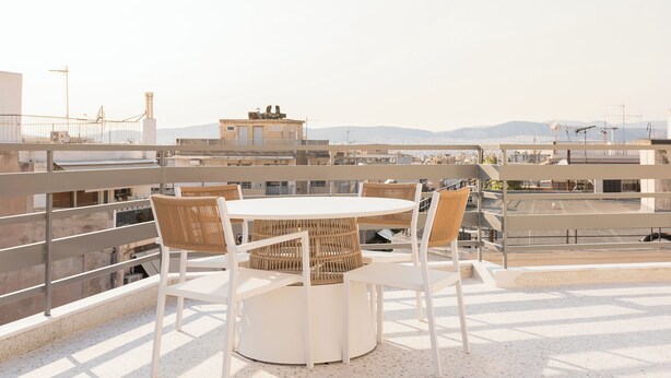 A rooftop terrace with a round table and wicker chairs, overlooking a cityscape with buildings and mountains. - SOL by Zoia Living (Athens)