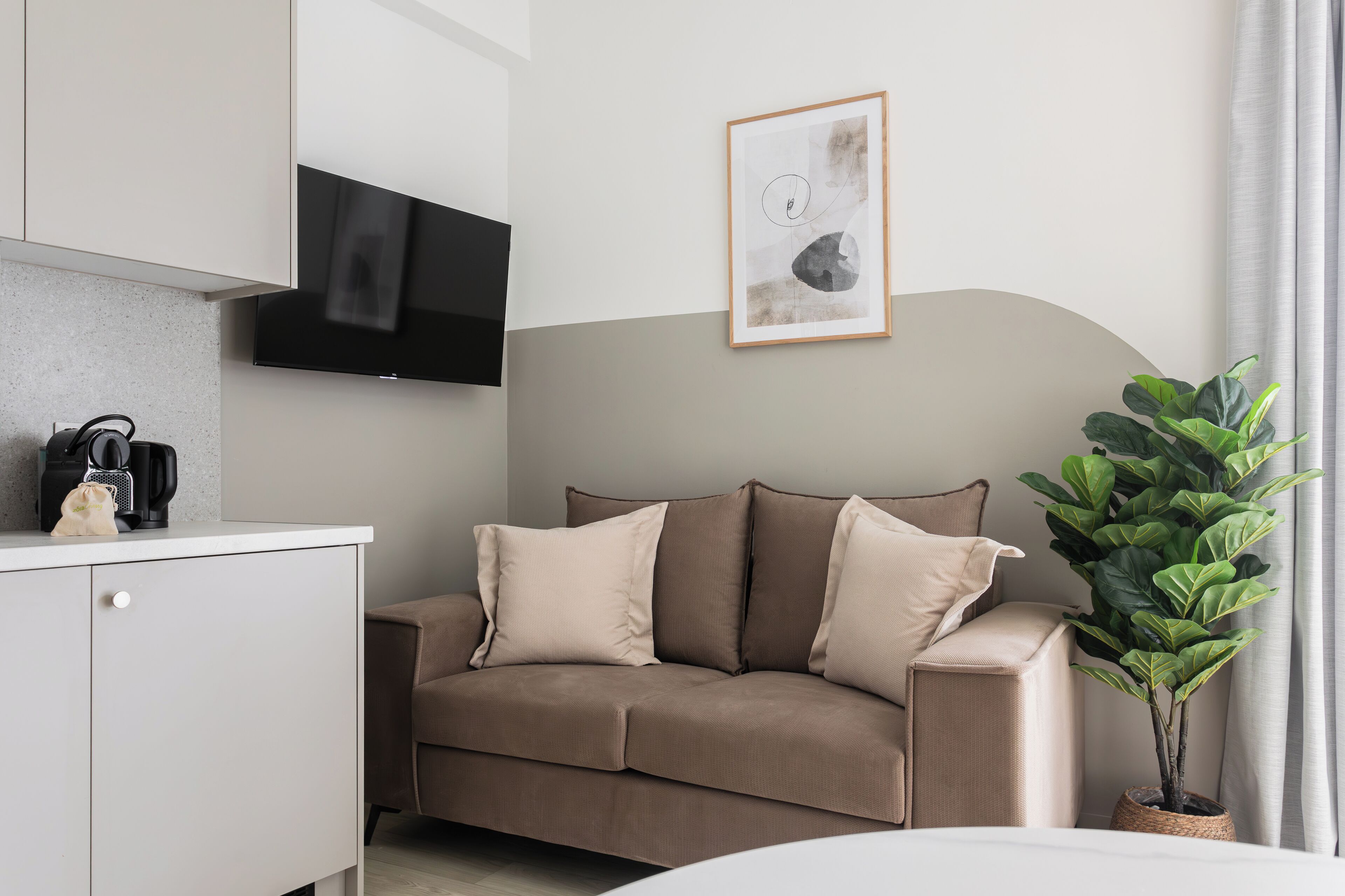 Un soggiorno moderno con divano, macchina del caffè, televisore e un quadro appeso al muro.