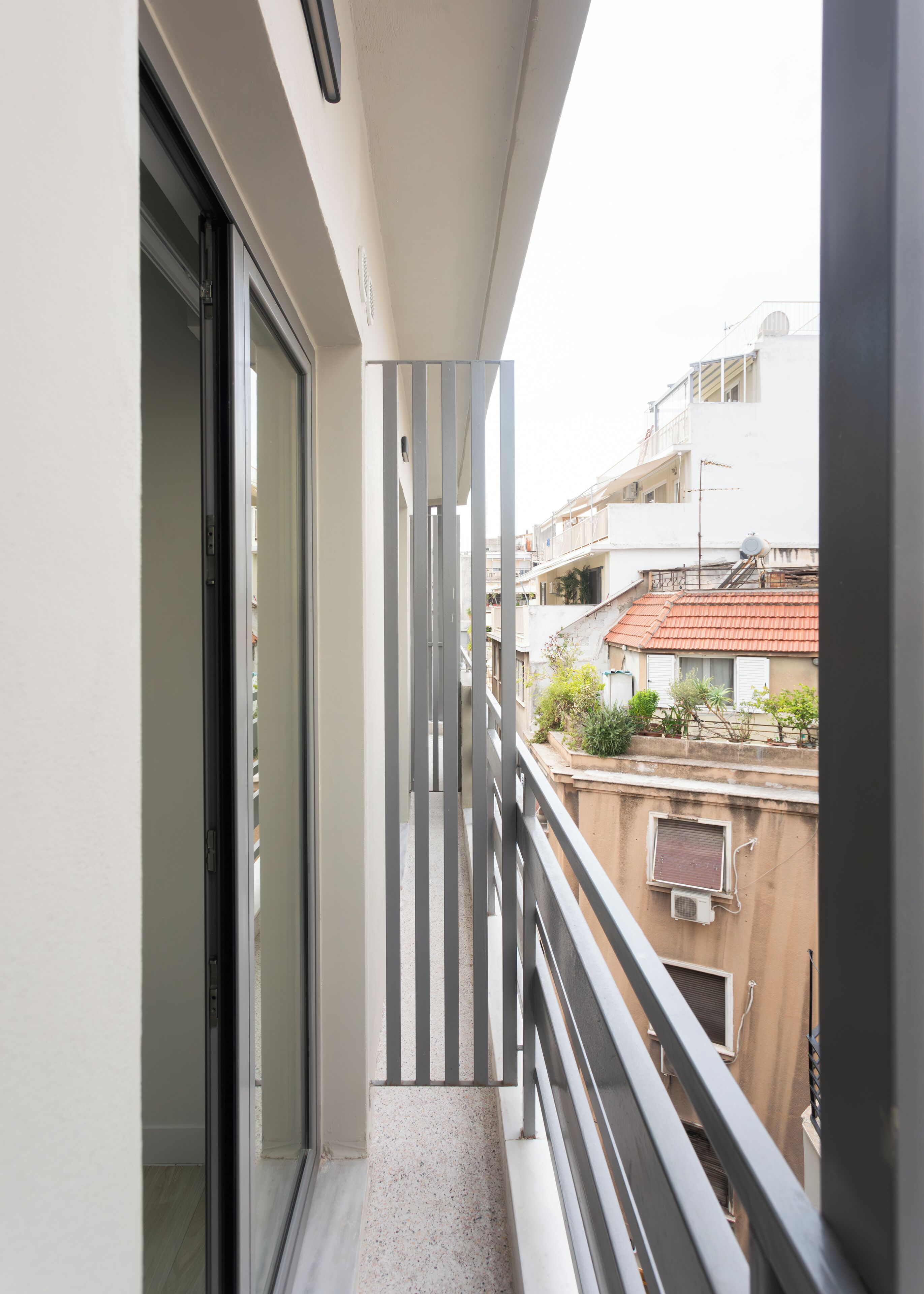 A narrow balcony with a metal railing, a sliding glass door, and a view of neighboring buildings.