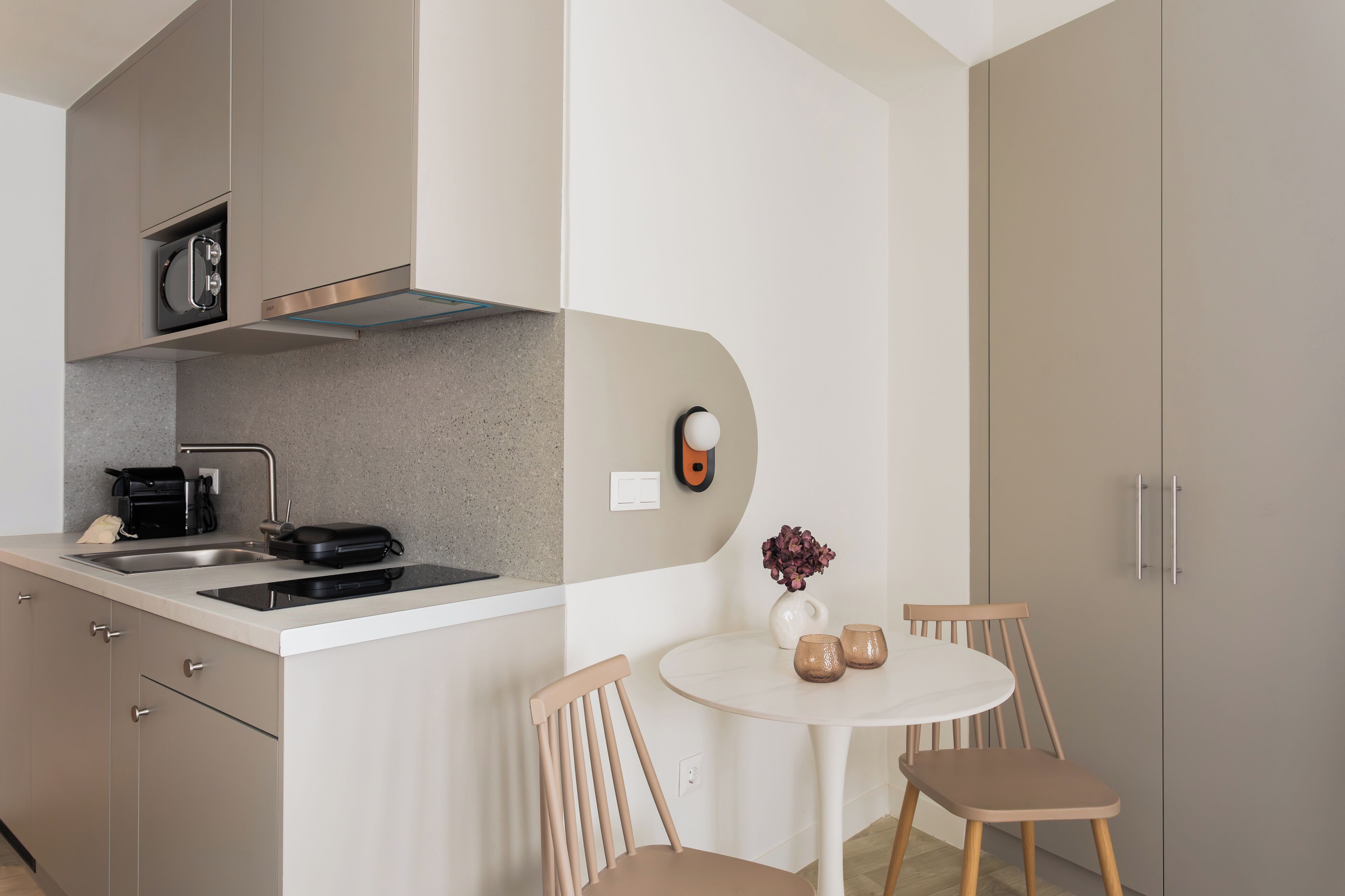 A modern kitchen with a built-in oven, a sink, and a small dining area with two chairs and a table.