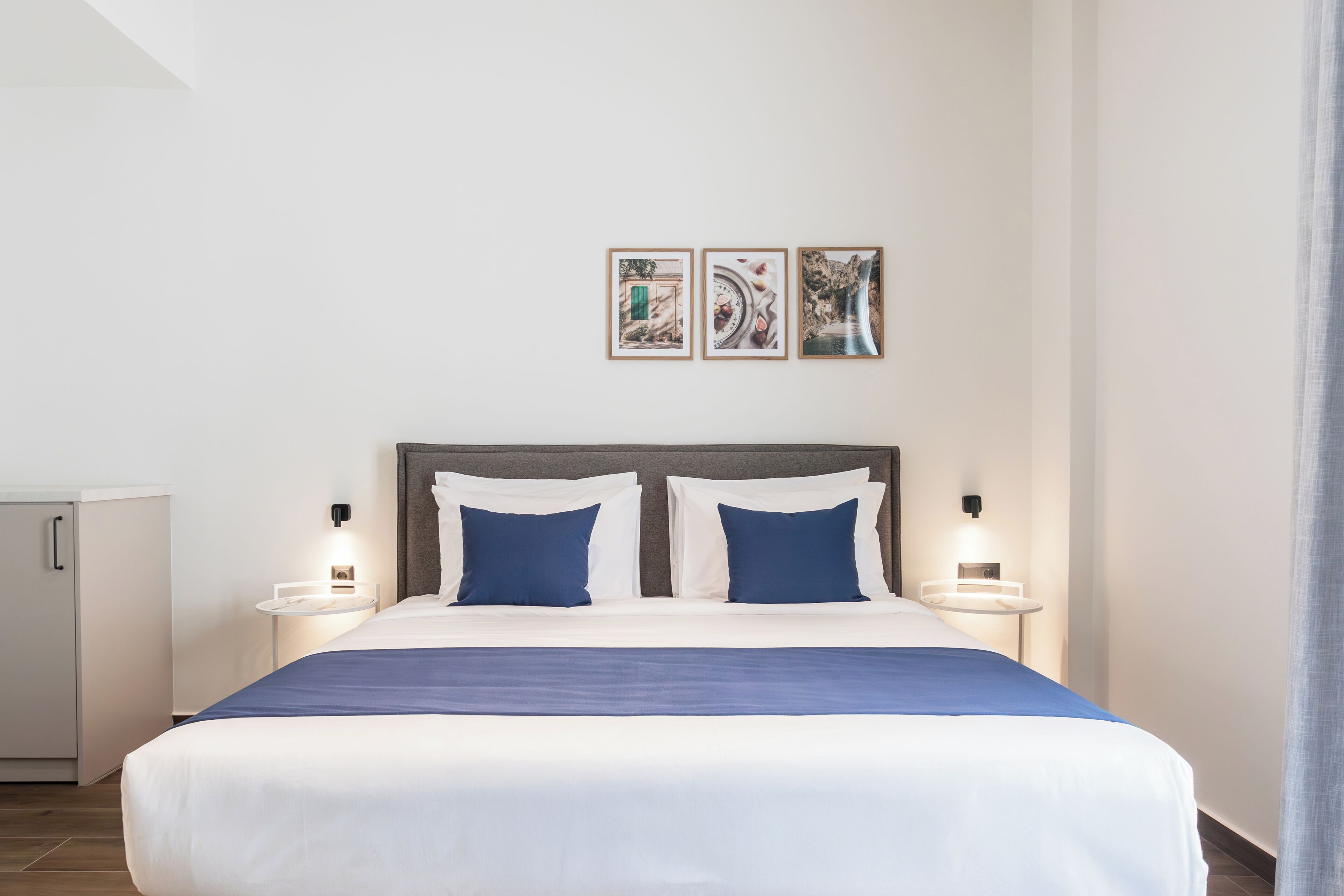A hotel room with a large bed, two bedside tables, a wardrobe, and three framed pictures on the wall.