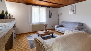 Una habitación acogedora con techo de madera, un sofá gris, una cama blanca y una mesita con un florero.