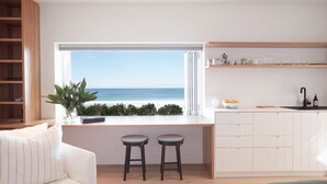Une cuisine moderne avec vue sur la mer, deux tabourets de bar, un canapé blanc et une bibliothèque en bois.