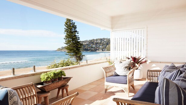 Un balcon avec vue sur la mer, des meubles en osier et des plantes en pot.