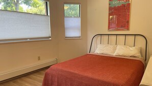 A bedroom with a bed, two windows, a radiator, and a map on the wall. - Mount Pleasant Garden Apartment (Vancouver)