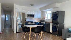 A modern kitchen with stainless steel appliances, a dining table with chairs, and a laundry area with a washing machine. - Mount Pleasant Garden Apartment (Vancouver)