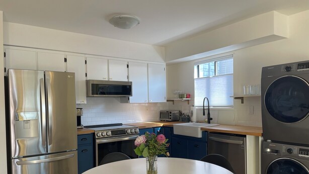 A modern kitchen with stainless steel appliances, a white dining table, and a vase of flowers. - Mount Pleasant Garden Apartment (Vancouver)