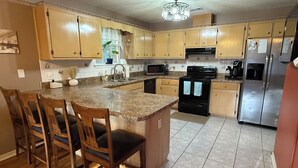 A kitchen with wooden cabinets, a granite countertop, a black stove, and a stainless steel refrigerator.