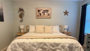 A neatly made bed with a white bedspread and pillows, flanked by two bedside tables with lamps, in a room with a world map artwork and a starfish decoration on the wall.