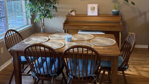 A dining area with a wooden table, six chairs, and a piano.