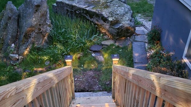 A wooden staircase leading to a garden area with a pathway, rocks, and plants.