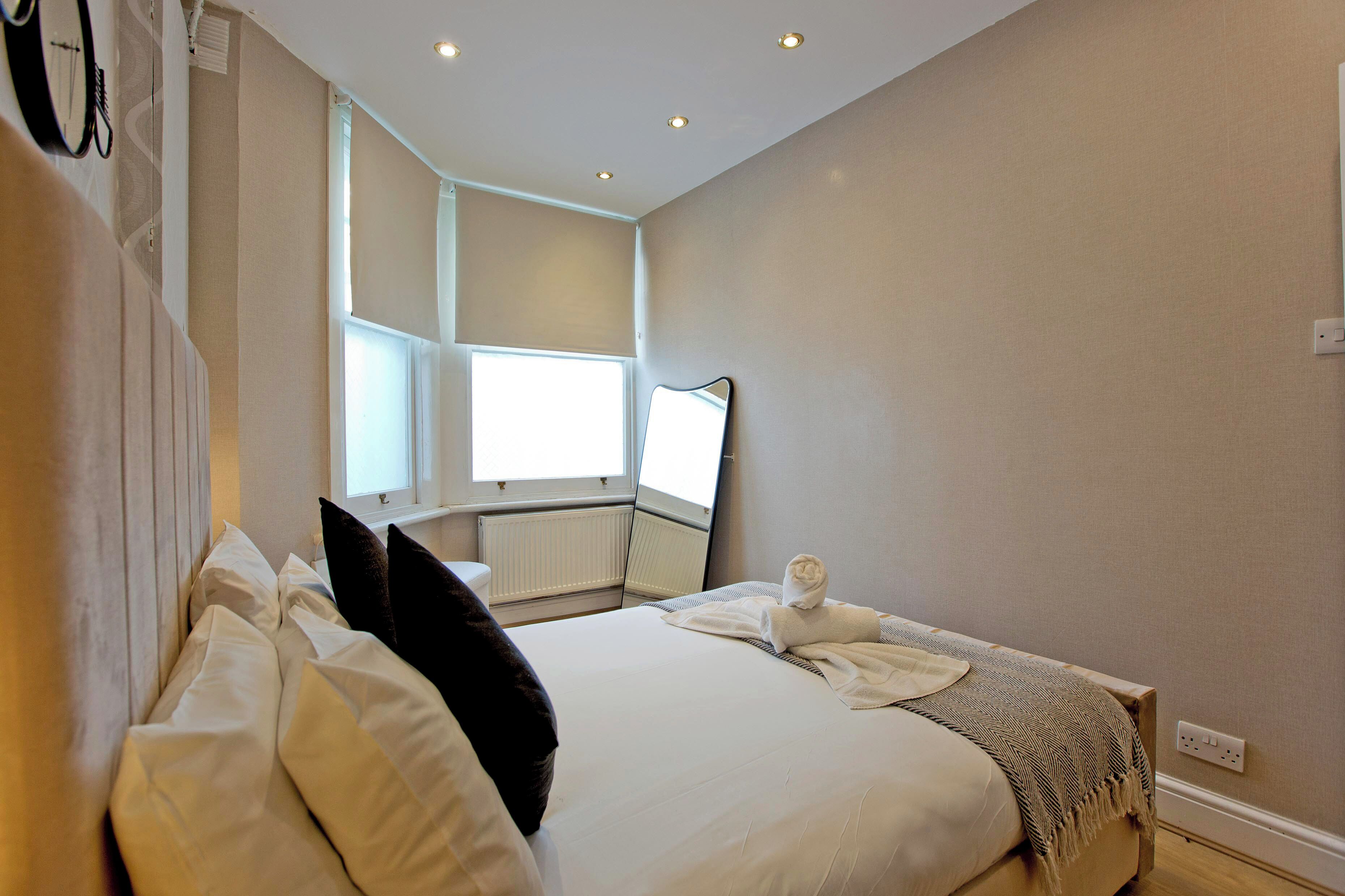 Une chambre d’hôtel avec un lit, une fenêtre, un radiateur et un miroir fixé au mur.