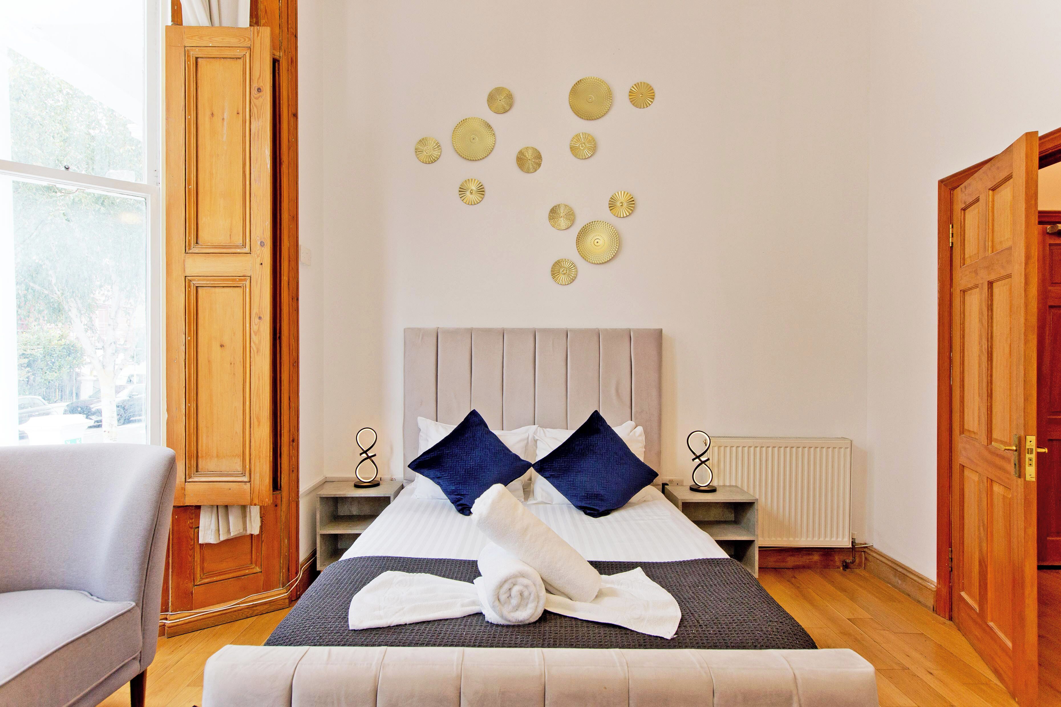 A neatly arranged hotel room with a bed, a chair, a wall with decorative plates, and a window.