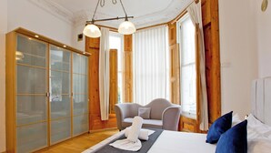 Hotellihuone, jossa on sänky, tuoli, vaatekaappi ja ikkuna, jossa on verhot.