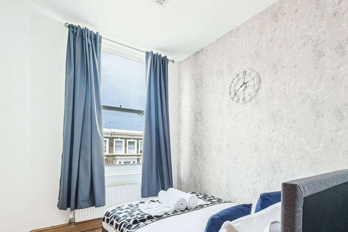 A bedroom with a large bed, a view of the city through a window, and a clock on the wall.
