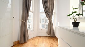 A room with a wooden floor, white walls, and a window with curtains. - Imperial Earls Court Apartments (London)
