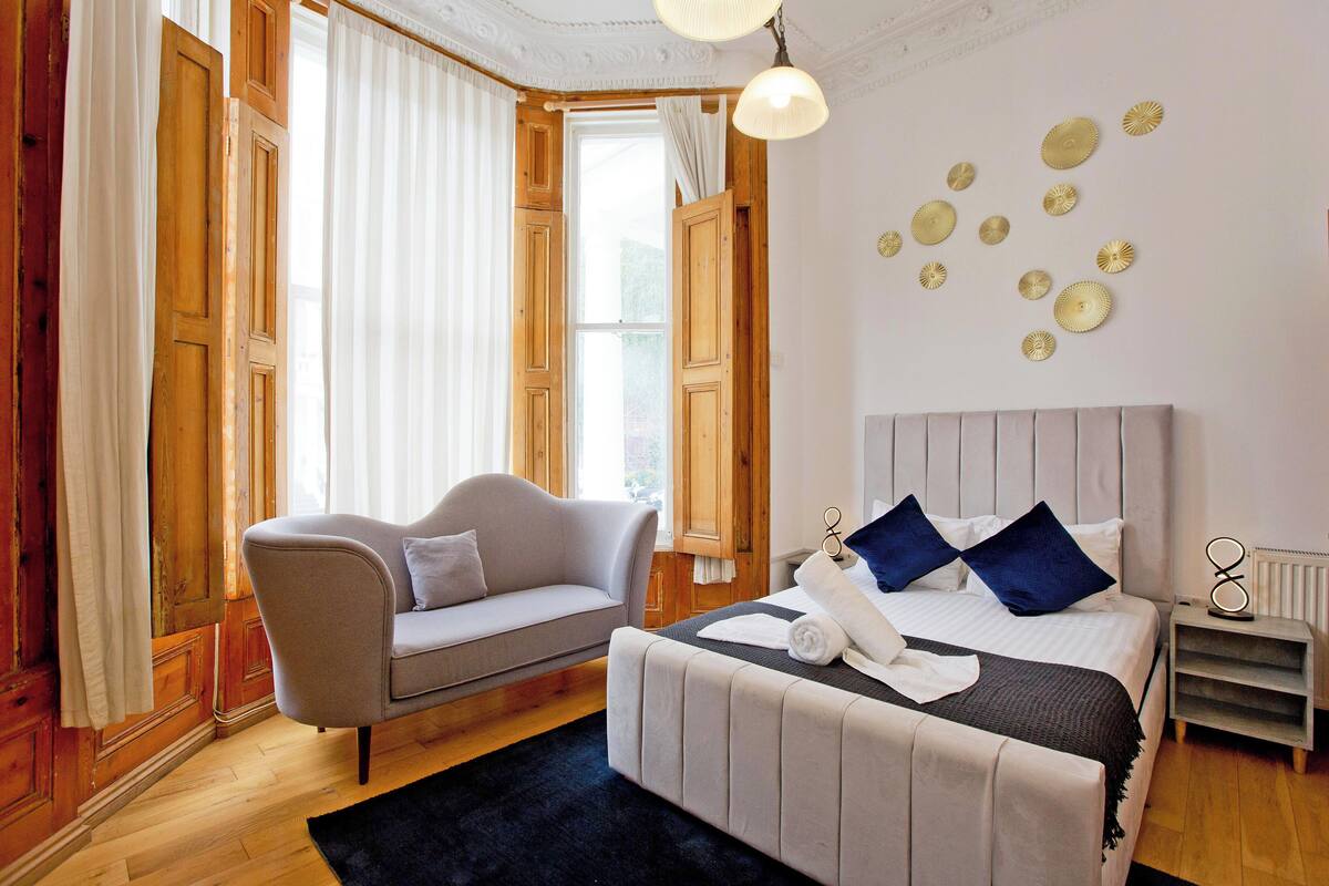 A bedroom with a bed, a sofa, a window with curtains, and a wall with decorative plates.