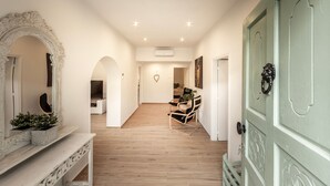 Un pasillo con suelo de madera, pared blanca y puerta verde. Hay un banco con una planta encima.