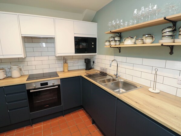 A modern kitchen with white cabinets, a Bosch oven, a microwave, a sink, and a wooden countertop. - The Loft Ystradgynlais (Swansea)