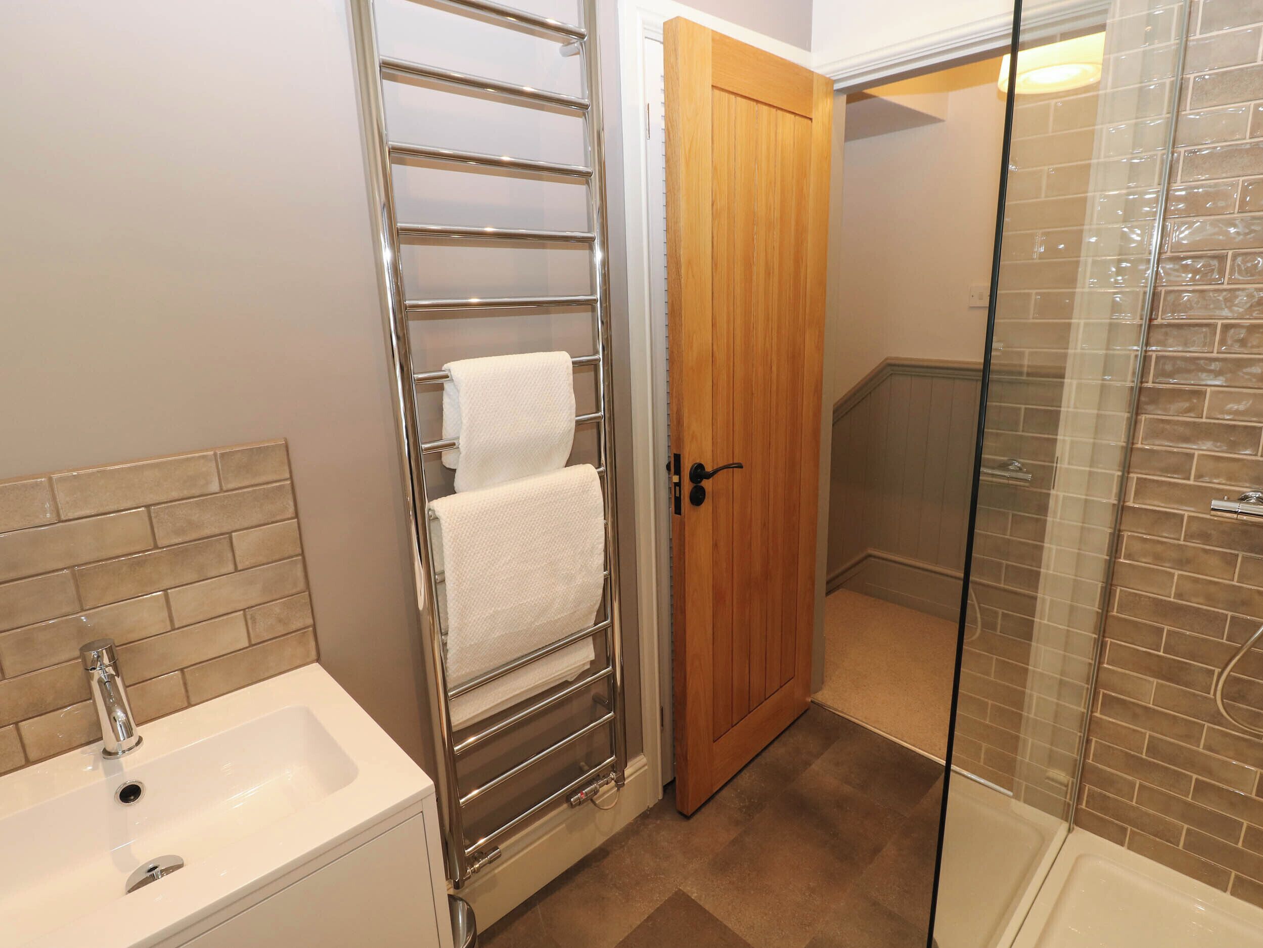 Une salle de bain équipée d’un lavabo, d’un porte-serviettes, d’une porte en bois et d’un espace douche.