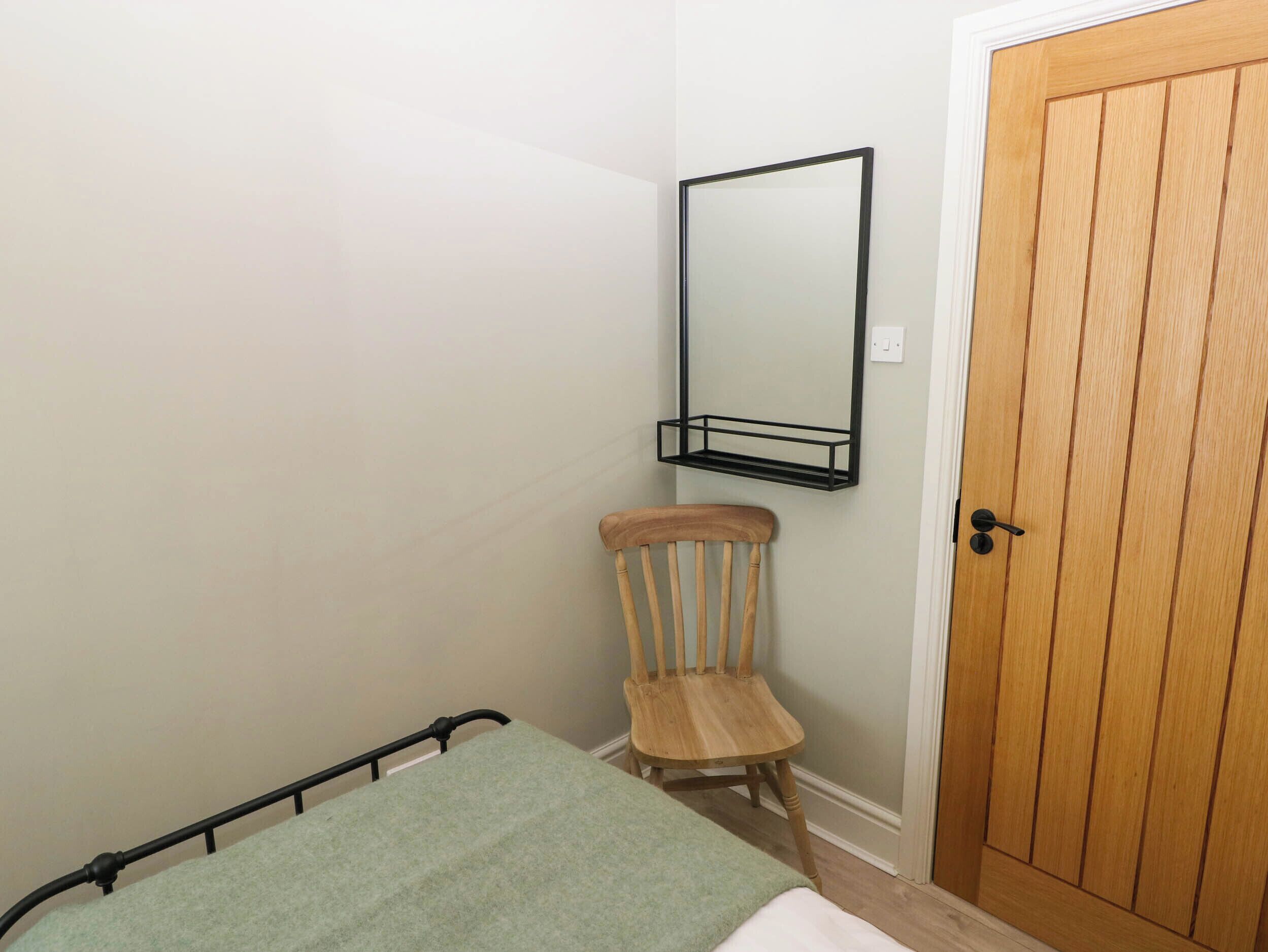 A bedroom with a bed, a wooden chair, a wooden door, and a wall-mounted shelf.