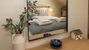 Un dormitorio con una cama, una mesita de noche con un cuenco, un pequeño modelo de casa y un espejo que refleja la habitación.