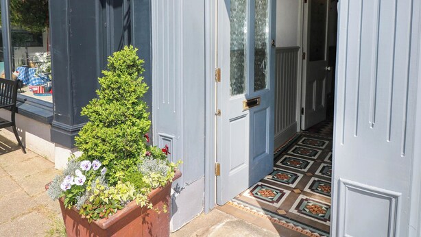 Una puerta azul con una placa de número, una planta en maceta con flores y un suelo con diseño.