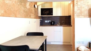 Un comedor con una mesa y sillas, una cocina con armarios blancos y una encimera negra, y una pared de piedra.