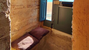 Una habitación pequeña y rústica con una cama individual, una ventana con vistas y una puerta.