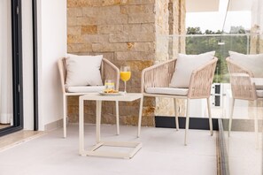 A modern outdoor seating area with wicker chairs and a small table, a glass of orange juice, and a stone wall backdrop. - Encanto da Foz - BY SCH (Foz do Arelho)
