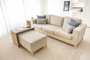 A modern living room with a beige sofa, a wooden coffee table, and a matching ottoman.