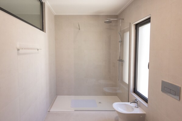 A modern bathroom with a walk-in shower, a sink, and a window providing natural light.