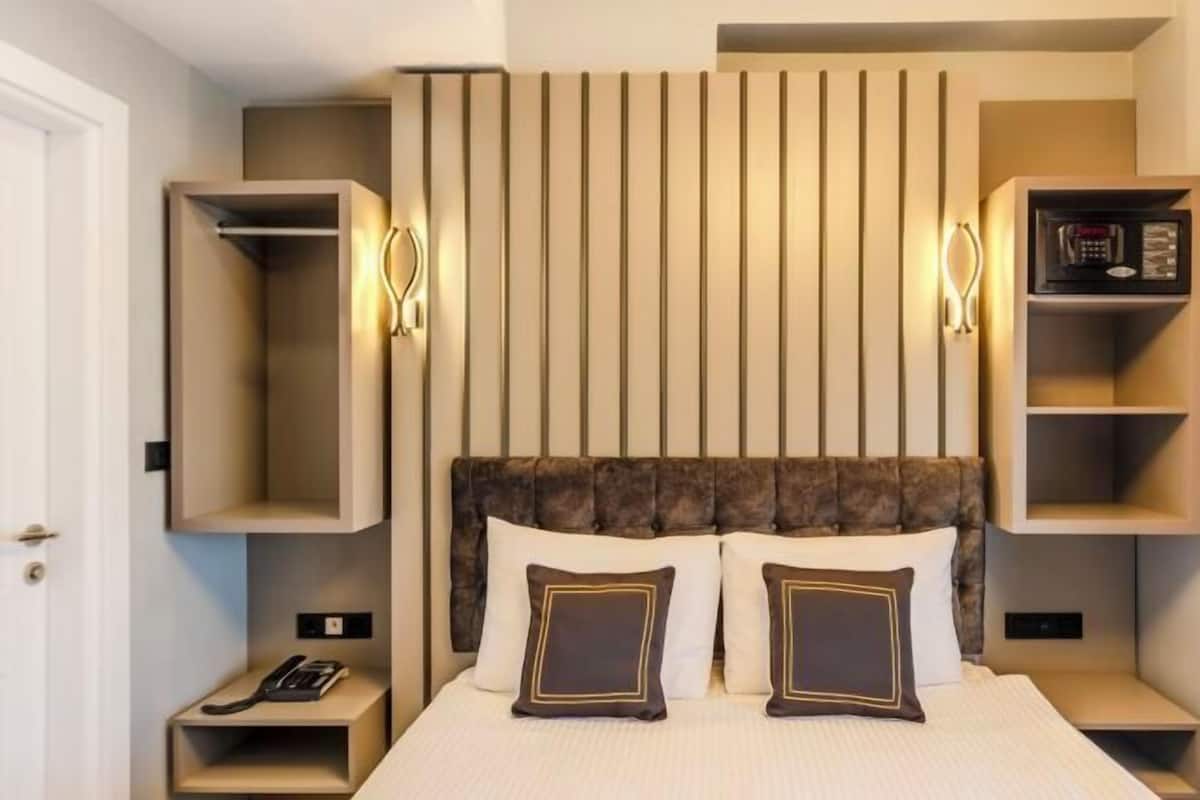 A modern hotel room with a large bed, two bedside tables, a built-in shelf, and a wall-mounted telephone.