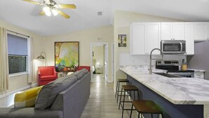 A modern kitchen with white cabinets, a microwave, and a stove. There is a gray sofa with a red chair and a colorful painting on the wall. - Charming 3BR in St. Augustine - Walk to Downtown, Near Beach, Wifi & A/C! (St. Augustine)