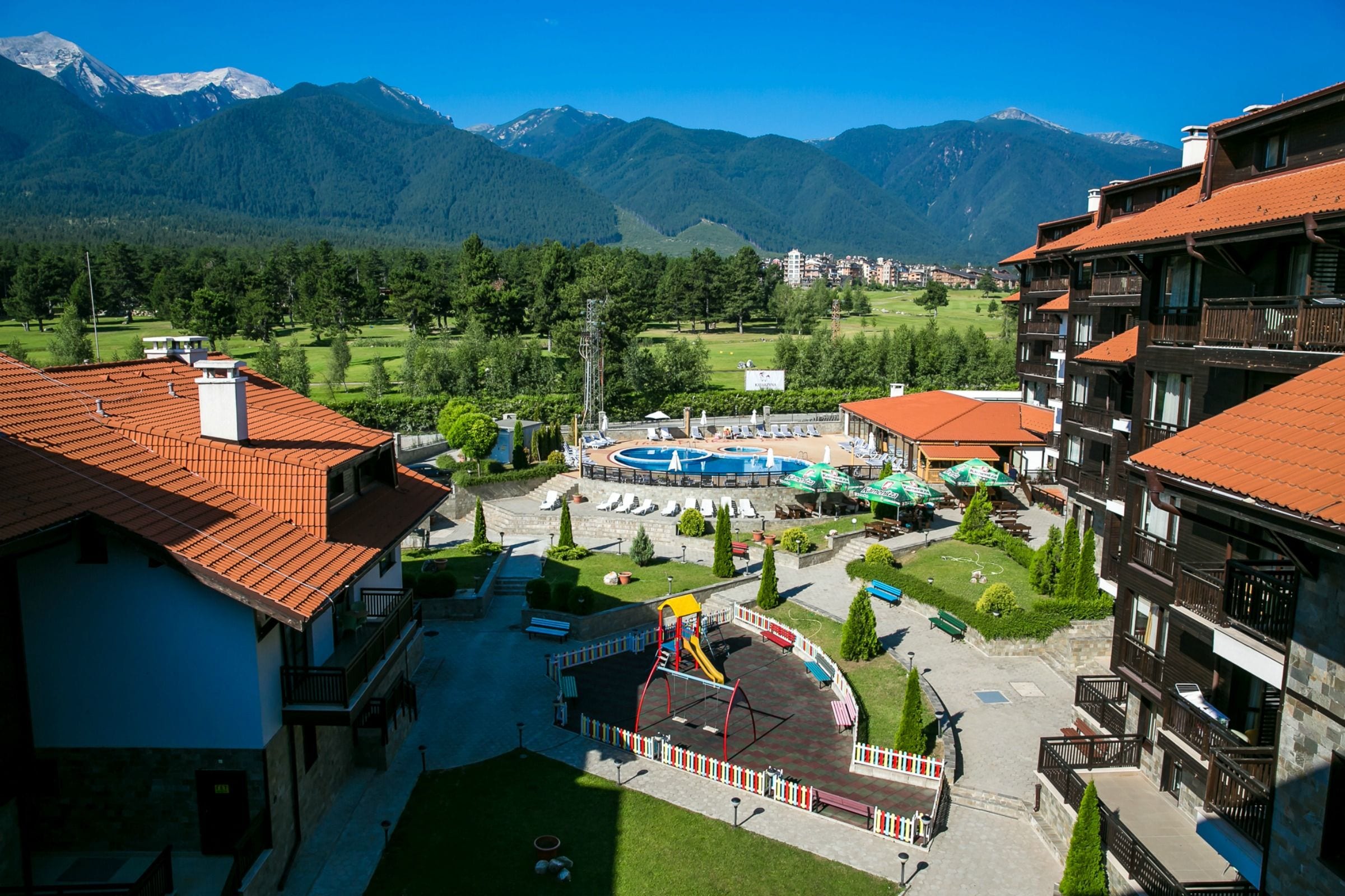 Un hotel con parque infantil, piscina y vistas a la montaña.