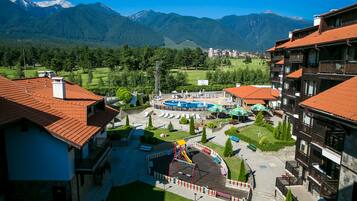 Un hotel con parque infantil, piscina y vistas a la montaña.