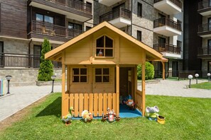 A small wooden playhouse with a picket fence, surrounded by a well-maintained lawn and a stone building in the background. - The Balkan Jewel Resort, Trademark Collection By W (Razlog)