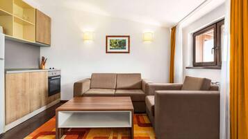 A compact living space with a sofa set, a coffee table, a kitchen area with cabinets and appliances, and a window with curtains.