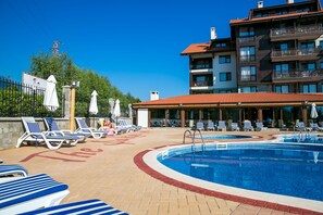 A swimming pool with lounge chairs and umbrellas, a covered seating area, and a multi-story building with balconies. - The Balkan Jewel Resort, Trademark Collection By W (Razlog)